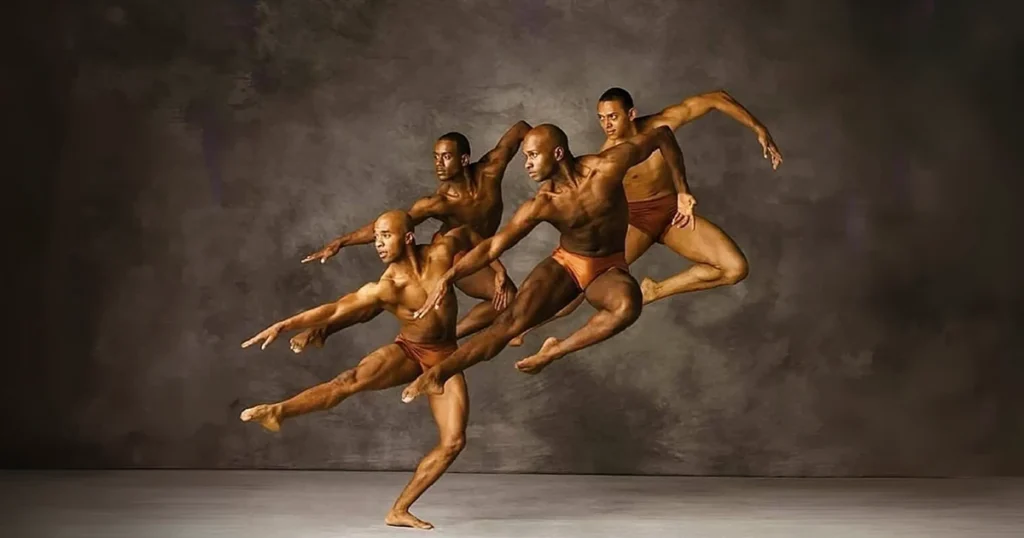 A photograph of muscular male dancers from the Alvin Ailey dance troupe executing a flawless, athletic leap, illustrating precision and perfectionism against a textured grey studio backdrop.